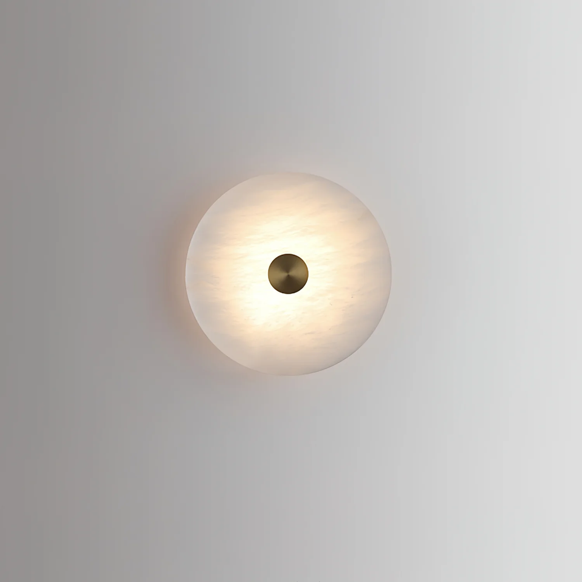 Lit disc alabaster wall light closeup pale neutral plaster wall minimalist shot