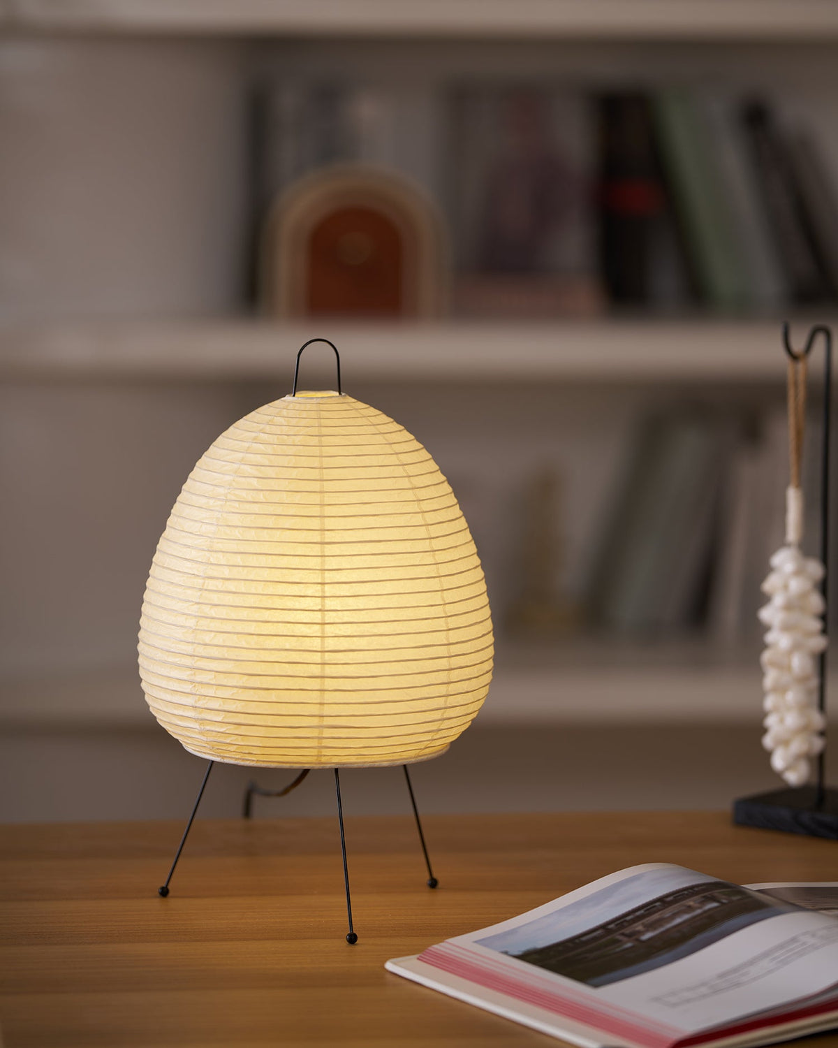 Akari Paper 1A Table Lamp on tabletop beside stacked magazines study nook