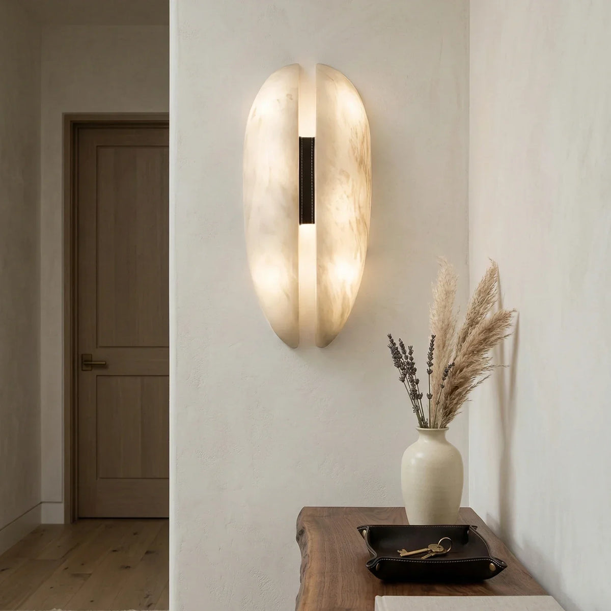 Glowing alabaster veil wall sconce on hallway wall above wooden console table