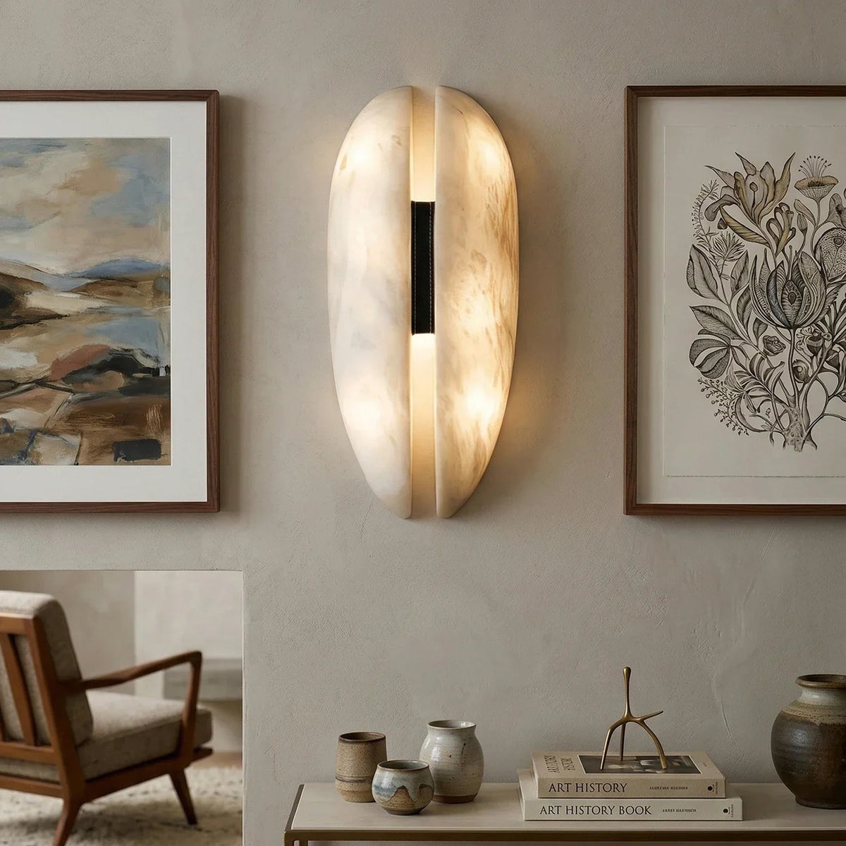 Warm lit split oval alabaster wall light hanging between framed art living room interior