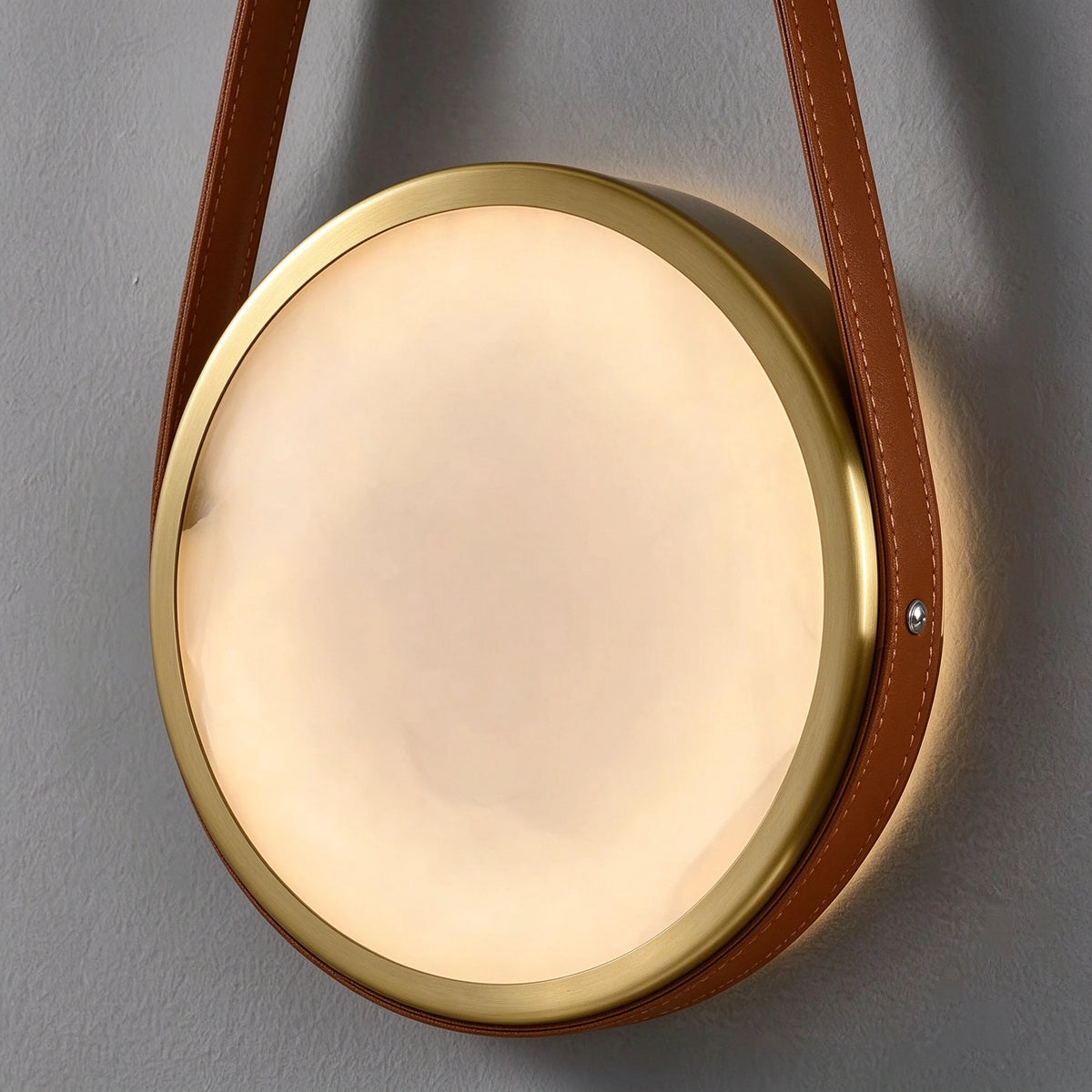 Illuminated Modern Leather Strap and Alabaster Disc Wall Sconce Studio Shot on Grey Background