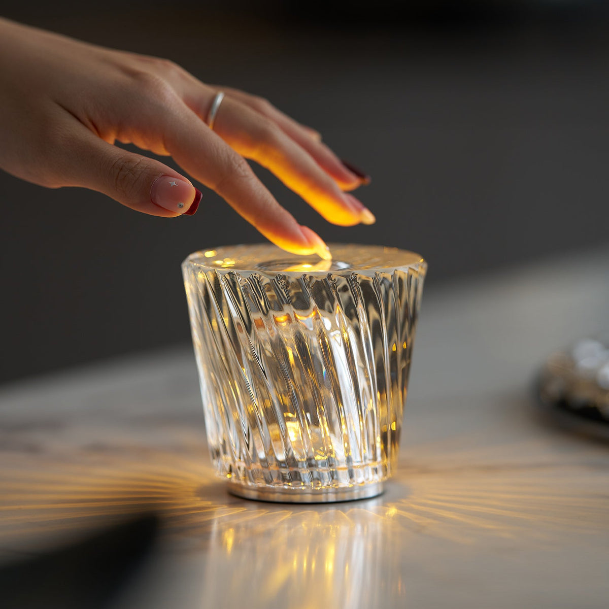 Hand touching illuminated Becrux crystal portable lamp on minimalist light tabletop