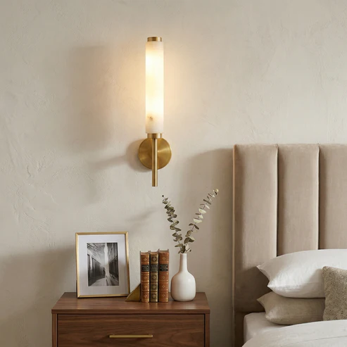 Lit Brindisi alabaster wall sconce brass finish mounted beside bed modern bedroom interior scene
