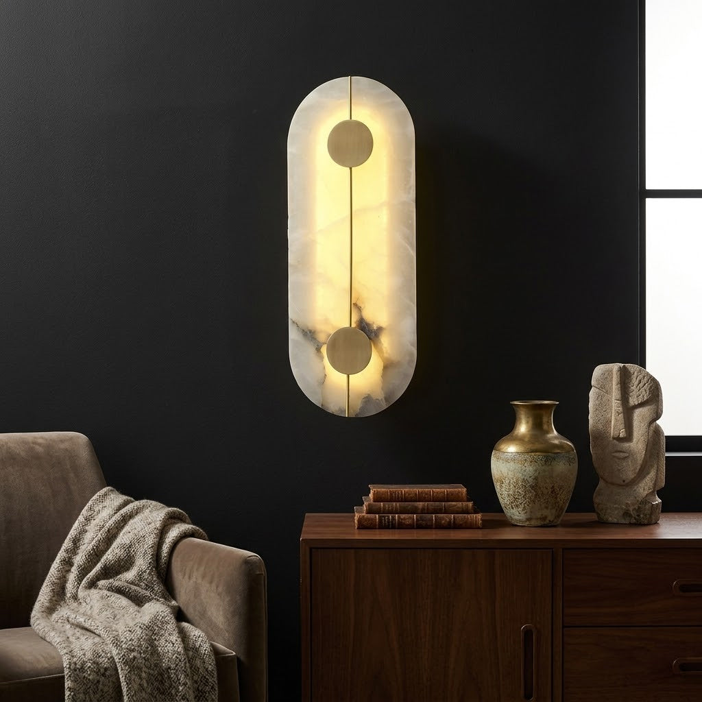 Lit oval Meridian alabaster wall sconce mounted on dark wall above wooden sideboard home styling