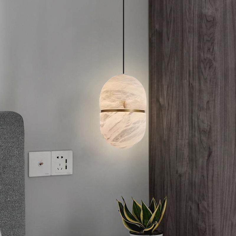 Lit Velo capsule alabaster pendant lamp mounted next to textured grey wall with succulent plant