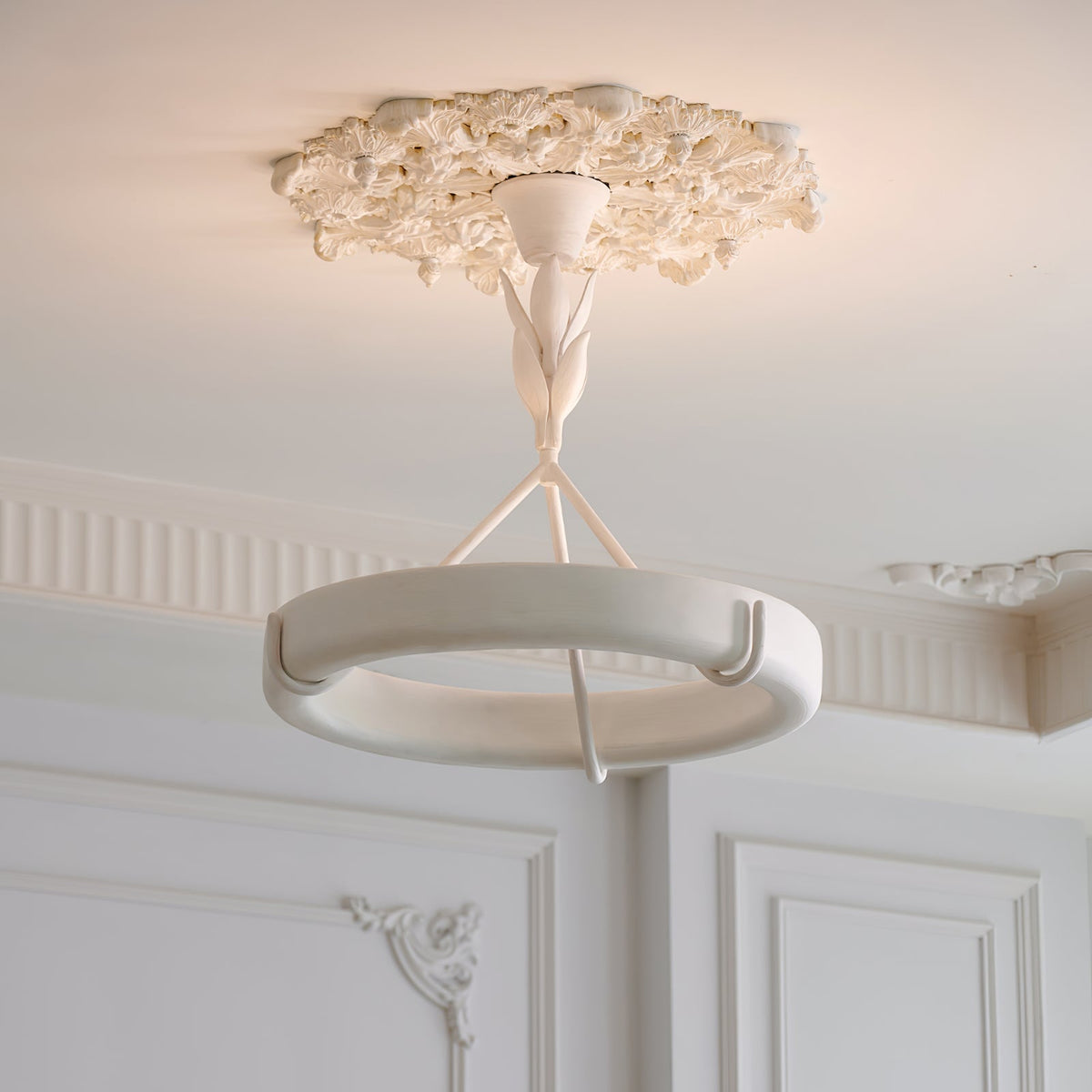 White plaster ring chandelier with floral carving, mounted in classic white decorative molding interior
